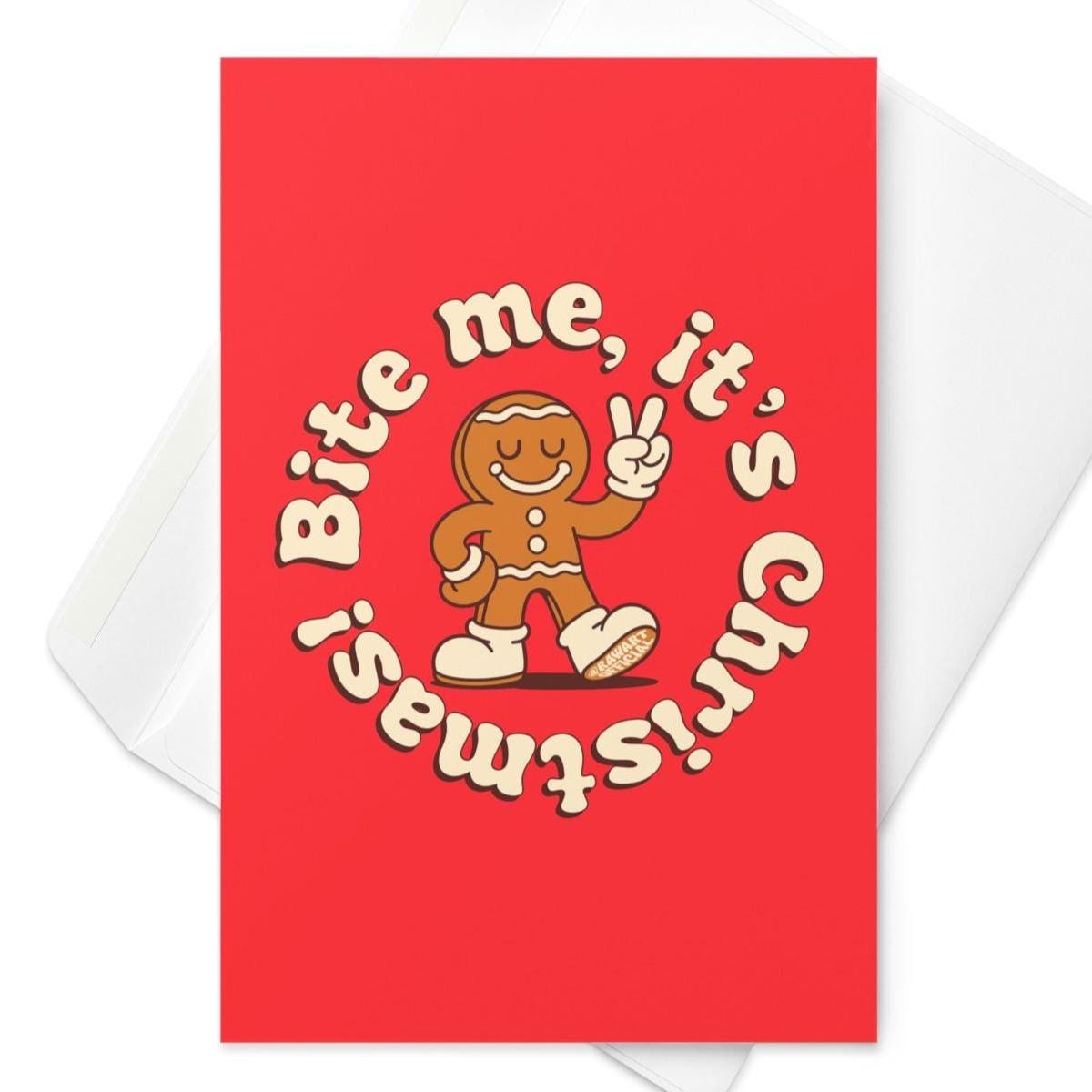 Red Christmas card featuring a smiling gingerbread man with a bite out of his leg, holding up a peace sign, surrounded by cream text reading “Bite me, it’s Christmas!”