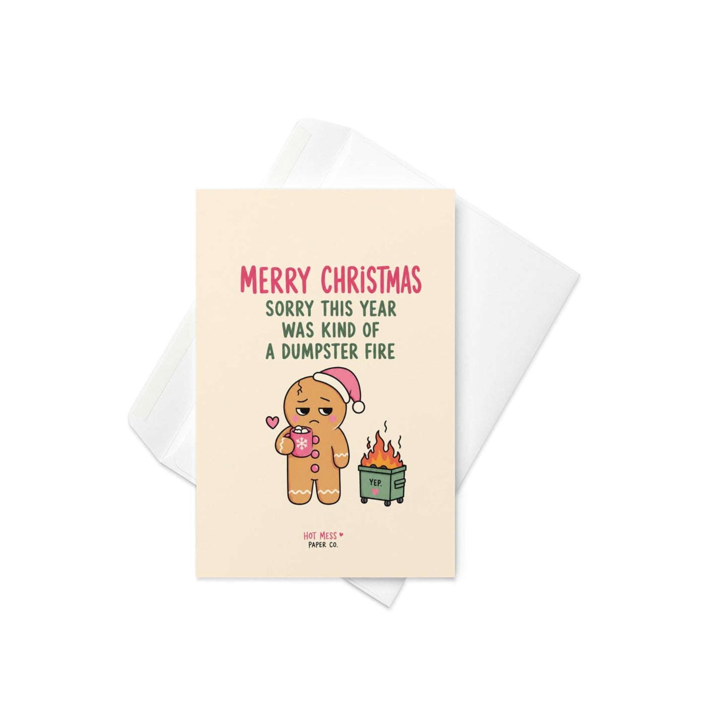 Funny Christmas card featuring a tired gingerbread cookie holding hot cocoa beside a tiny flaming dumpster with the phrase “Sorry This Year Was Kind Of A Dumpster Fire.”