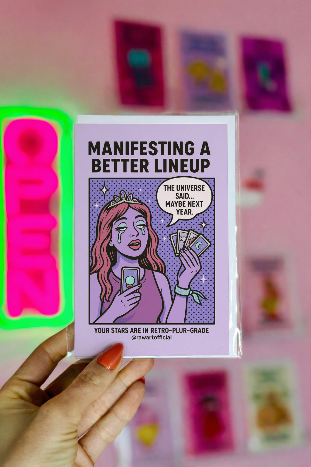 Card with text 'Manifesting a Better Lineup' held by a hand against a pink background with other cards.