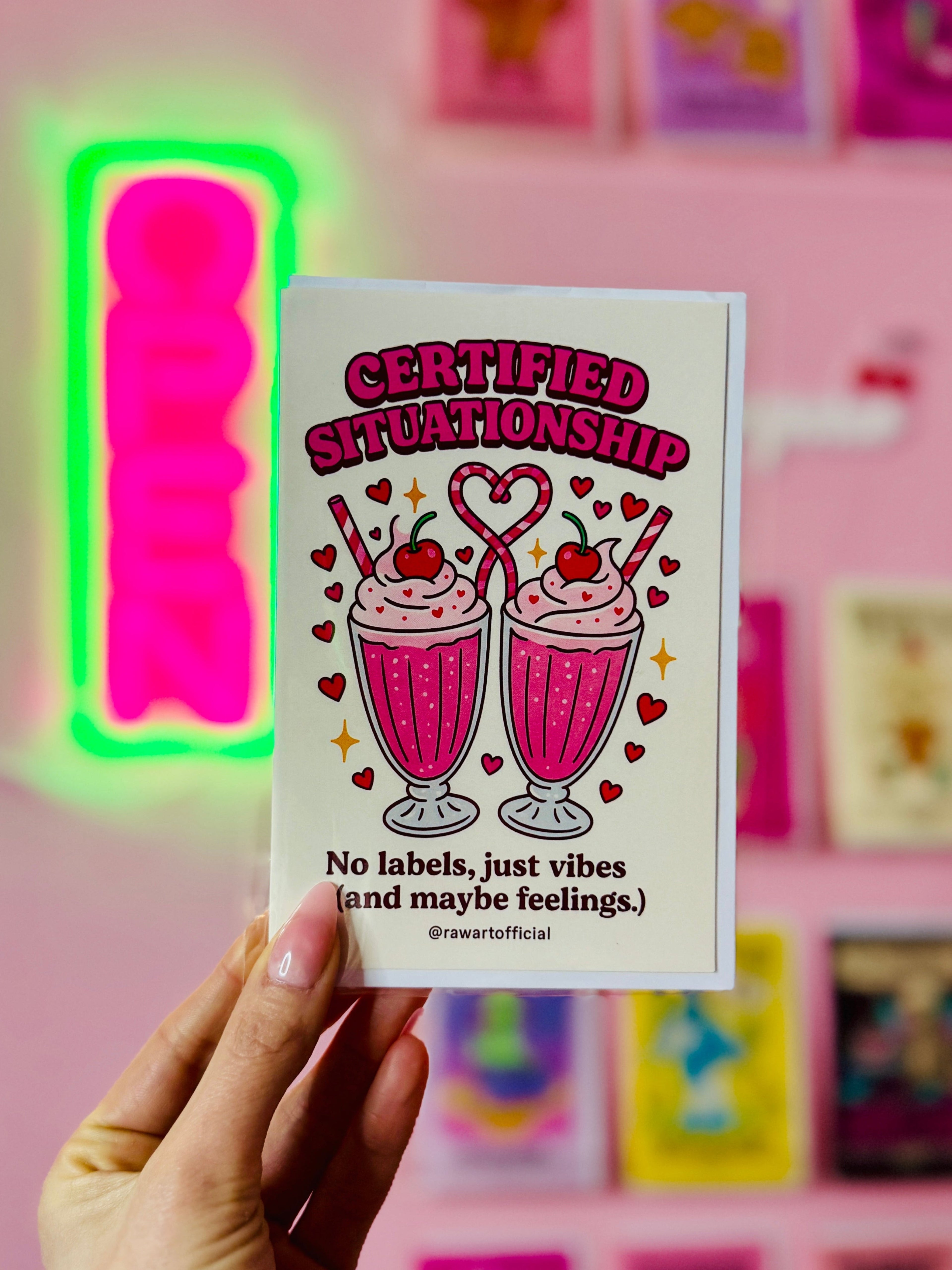 Hand holding a card with 'Certified Situationship' design against a colorful wall.