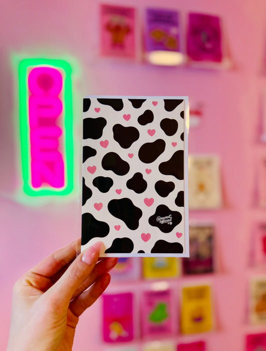 Cute cow print card with dark cow spots and scattered pink hearts aesthetic pattern design on cream background