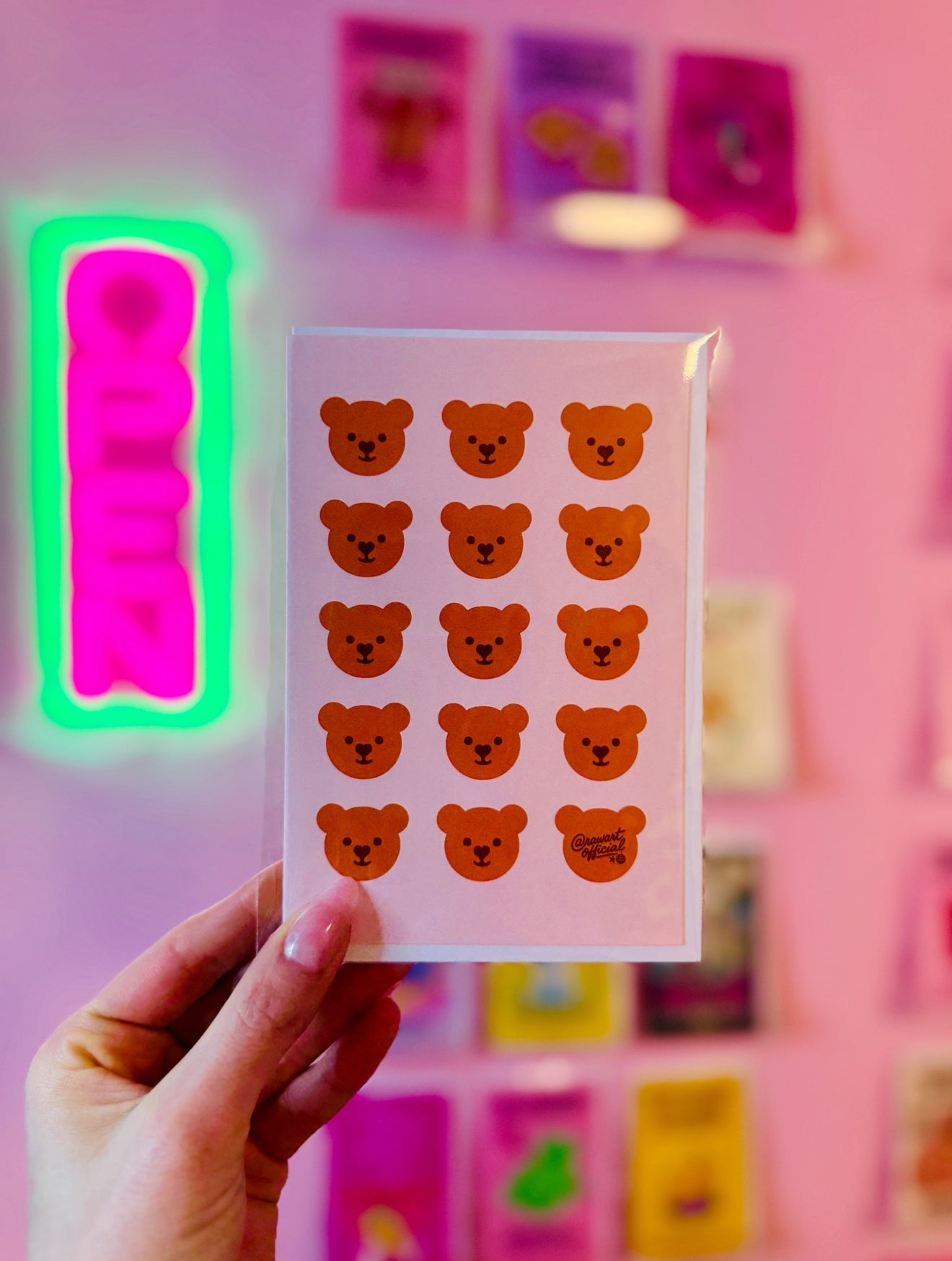 Pink card with repeating kawaii teddy bear faces in rows, one signed @rawartofficial.