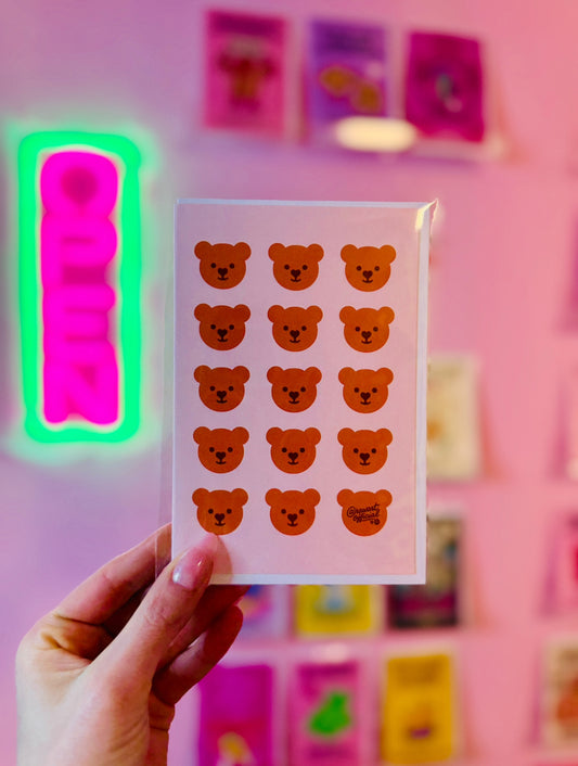 Pink card with repeating kawaii teddy bear faces in rows, one signed @rawartofficial.