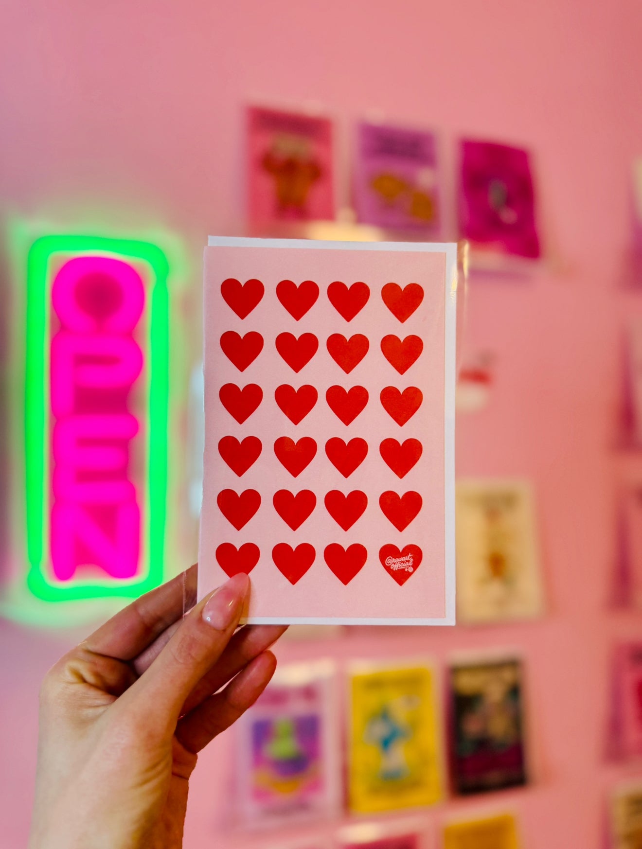 Pink card with repeating red heart pattern and one heart signed @rawartofficial.
