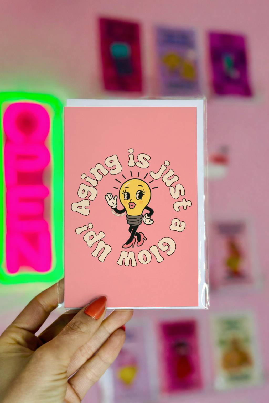 Pink birthday card featuring stylish lightbulb in heels with circular text “Aging Is Just a Glow Up.”