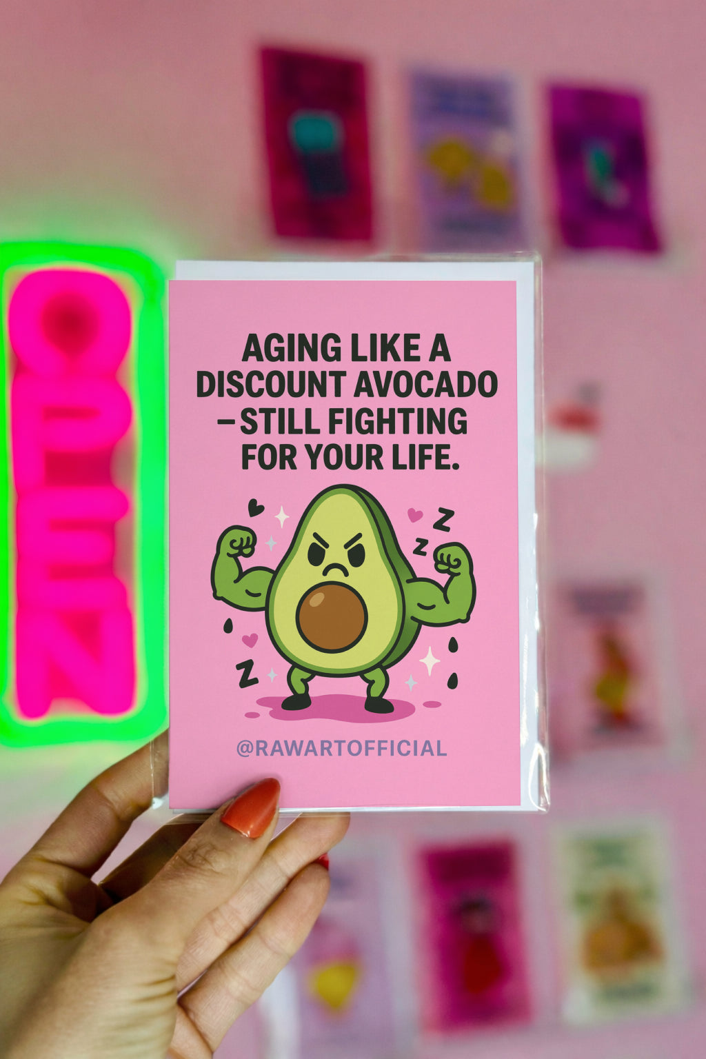 “Funny avocado birthday card featuring a muscular cartoon avocado flexing with a grumpy face on a pink background, illustrated by @rawartofficial.”