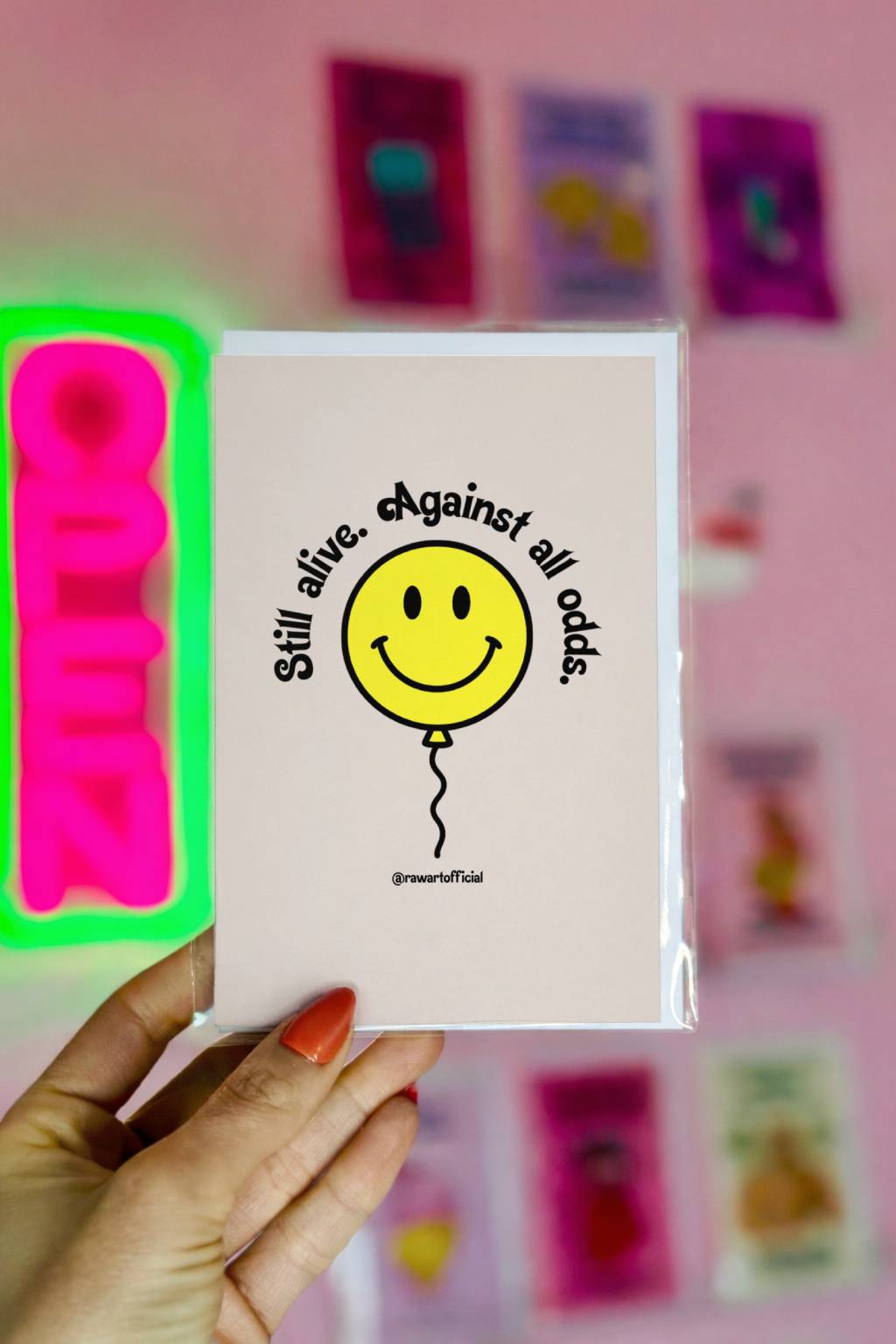 Cream birthday card featuring yellow smiley balloon and curved text reading “Still alive. Against all odds.”
