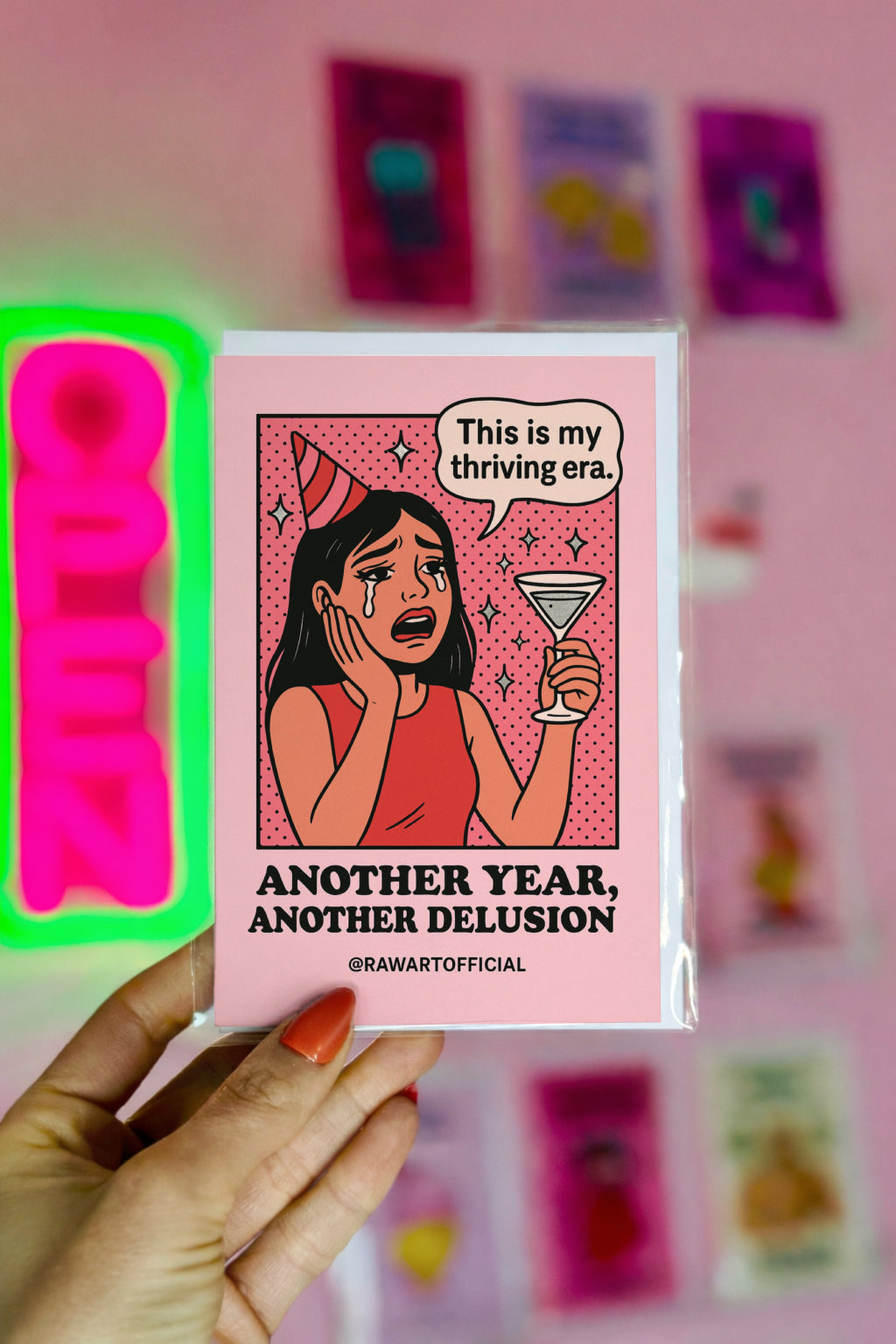 Crying cartoon woman in a red party hat holding a martini glass, saying “This is my thriving era,” with text “Another Year, Another Delusion” below.