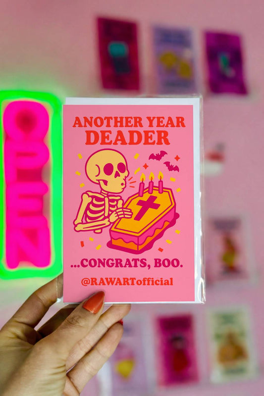 Pink skeleton birthday card with coffin cake and candles, reading “Another Year Deader …Congrats, Boo.”