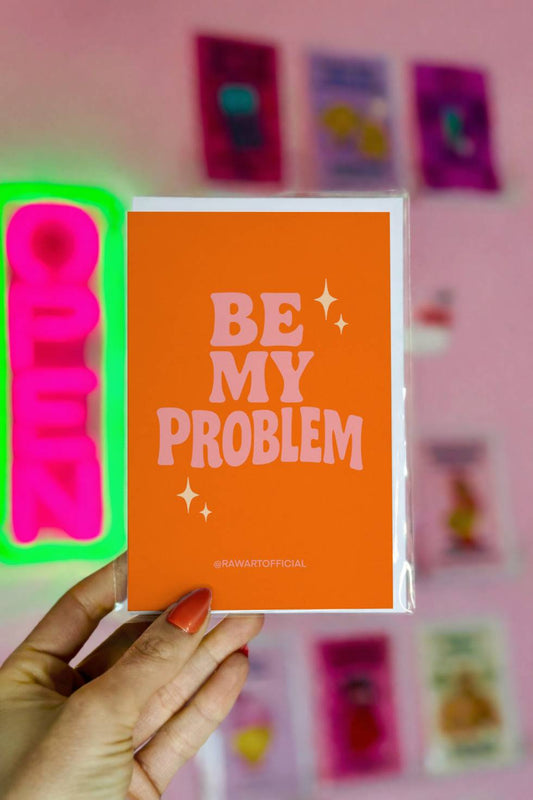 Greeting card with retro pink lettering reading “Be My Problem” on an orange background.