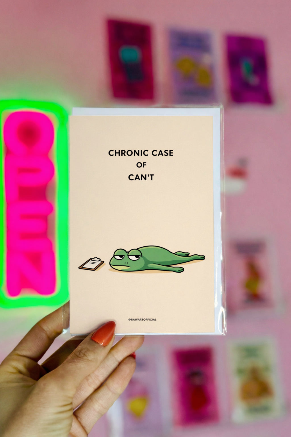 Notebook with a frog illustration and text held by a hand against a pink background with colorful cards.
