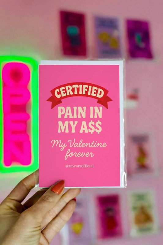 Funny greeting card reading “Certified Pain in My Ass, My Valentine Forever” on a bright pink background with retro lettering.