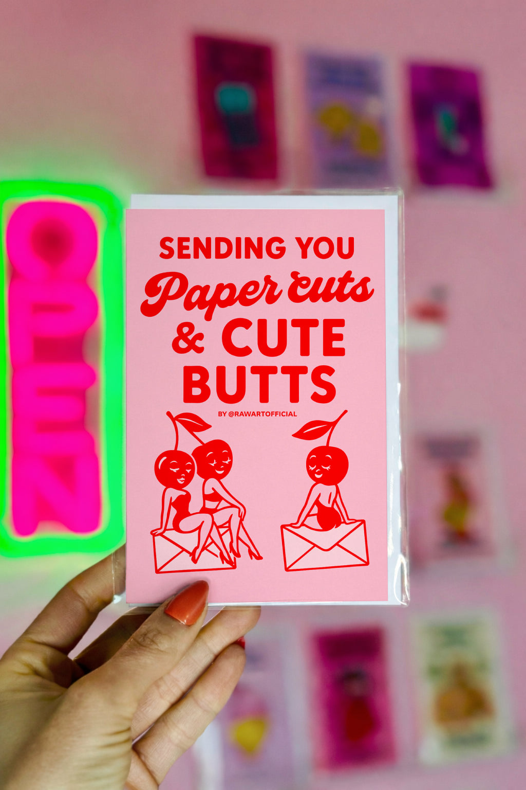 Retro pink and red greeting card with cherry pin-up characters sitting on envelopes, text reads “Sending You Paper Cuts & Cute Butts.”