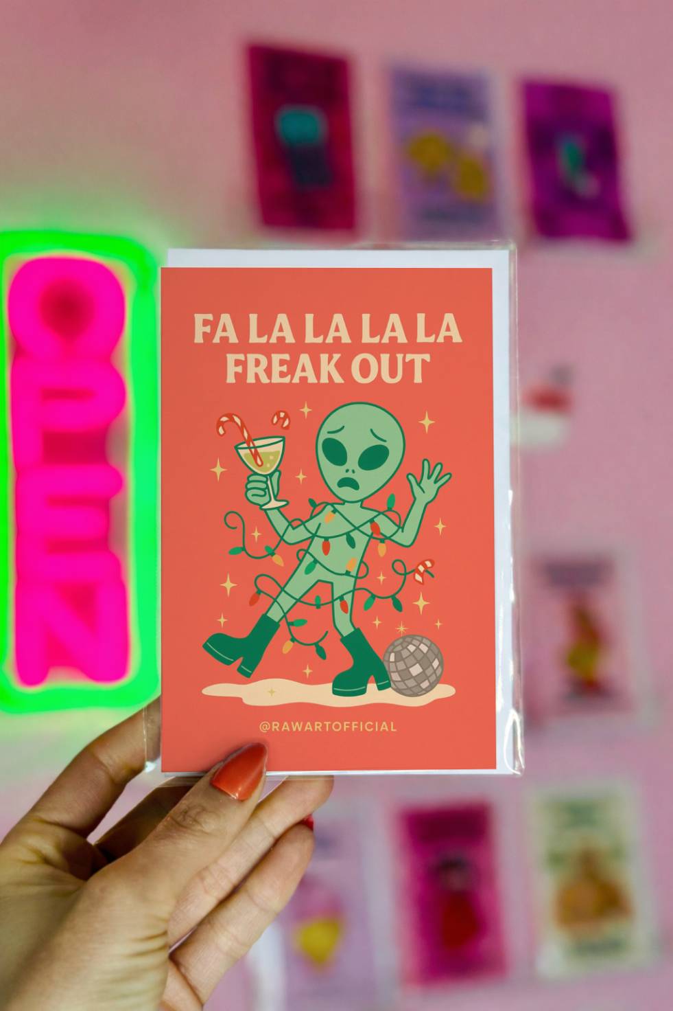 Funny alien Christmas card featuring an alien tangled in Christmas lights holding a cocktail with text “Fa La La La La Freak Out.”