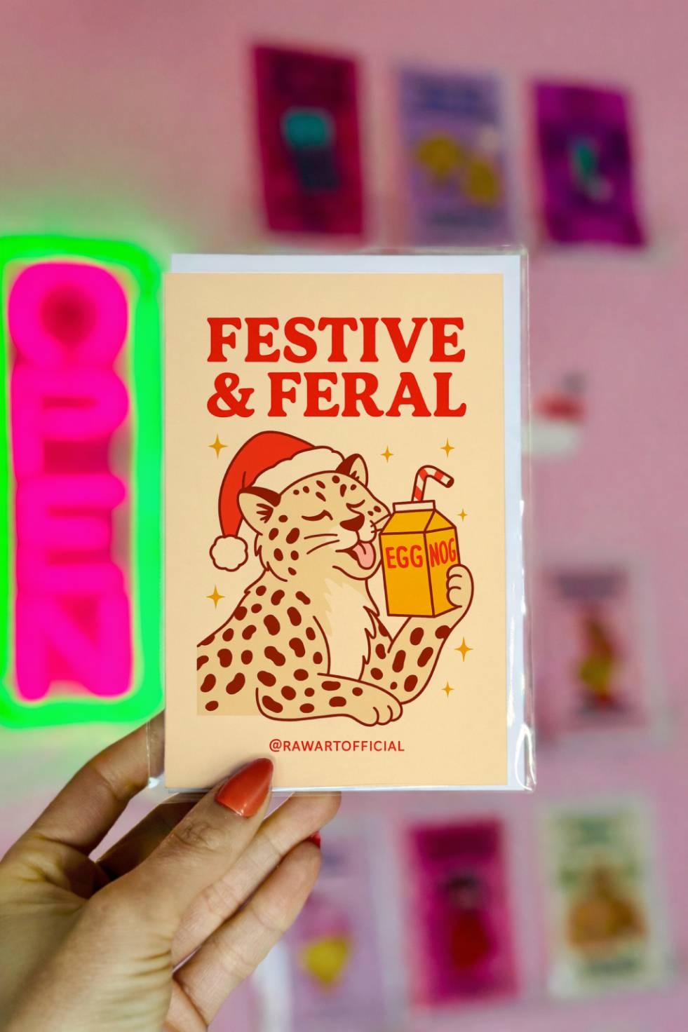 Funny Christmas greeting card featuring a leopard wearing a Santa hat drinking eggnog with the phrase “Festive and Feral.”