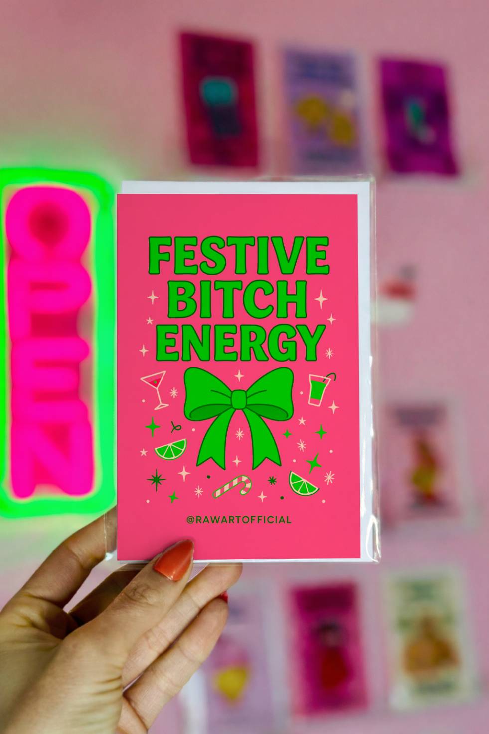 Funny Christmas greeting card with bold text reading “Festive Bitch Energy” and a green bow with cocktail and candy cane icons on a pink background.