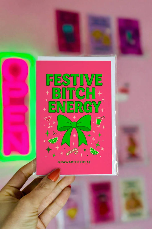 Funny Christmas greeting card with bold text reading “Festive Bitch Energy” and a green bow with cocktail and candy cane icons on a pink background.