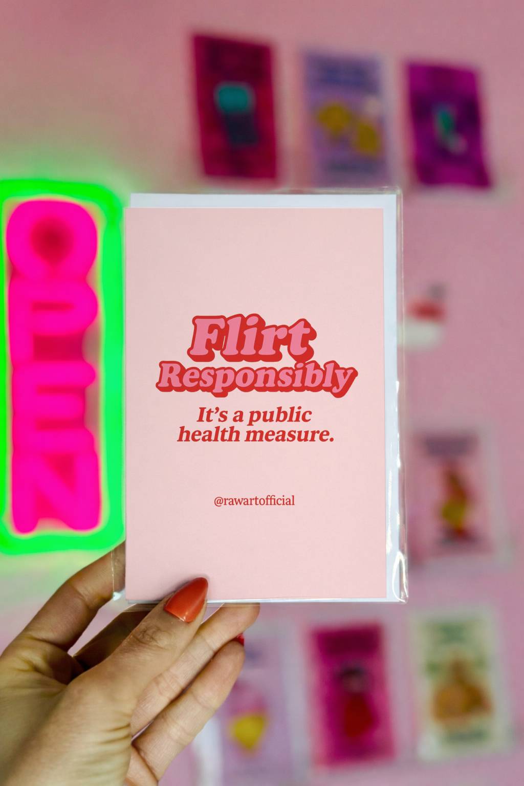 Pink greeting card with bold red retro text reading Flirt Responsibly It’s a Public Health Measure and @rawartofficial signature.