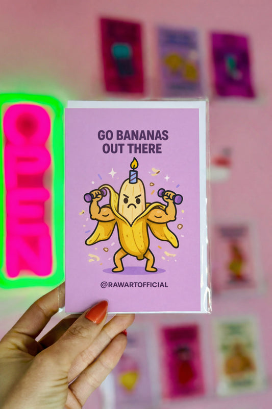Card with a cartoon banana character holding candles and text 'Go bananas out there' held by a hand against a pink background.
