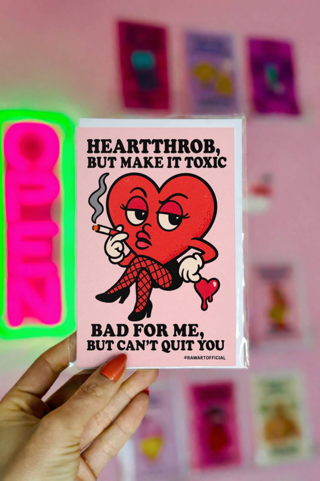 Pink greeting card reading Heartthrob But Make It Toxic Bad For Me But Can’t Quit You with sultry heart illustration, @rawartofficial signature.