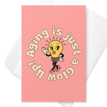 Pink birthday card featuring stylish lightbulb in heels with circular text “Aging Is Just a Glow Up.”