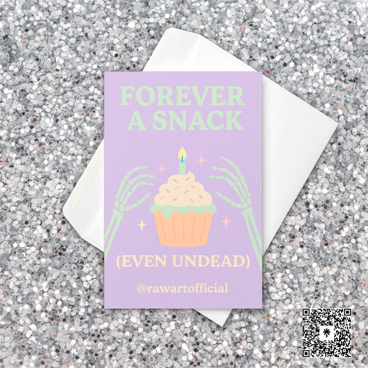 Halloween card with skeleton hands holding cupcake and text “Forever a Snack (Even Undead)” in pastel purple and green.