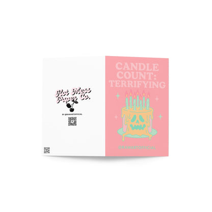 Pink greeting card that reads ‘CANDLE COUNT: TERRIFYING’ above a melting skull-faced birthday cake with many lit mint candles and sparkles—spooky, pastel-goth vibe.