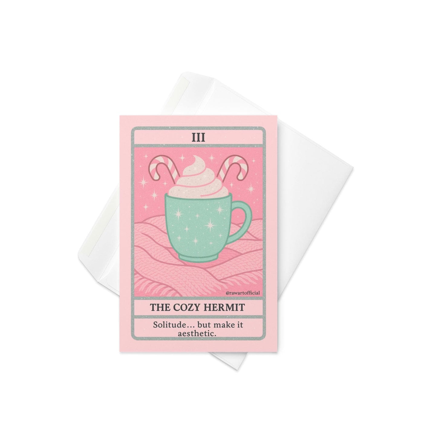 Pastel pink and mint Christmas tarot-style card featuring a mint green mug topped with whipped cream and candy canes on a pink knit blanket, titled “The Cozy Hermit” with the phrase “Solitude… but make it aesthetic.”