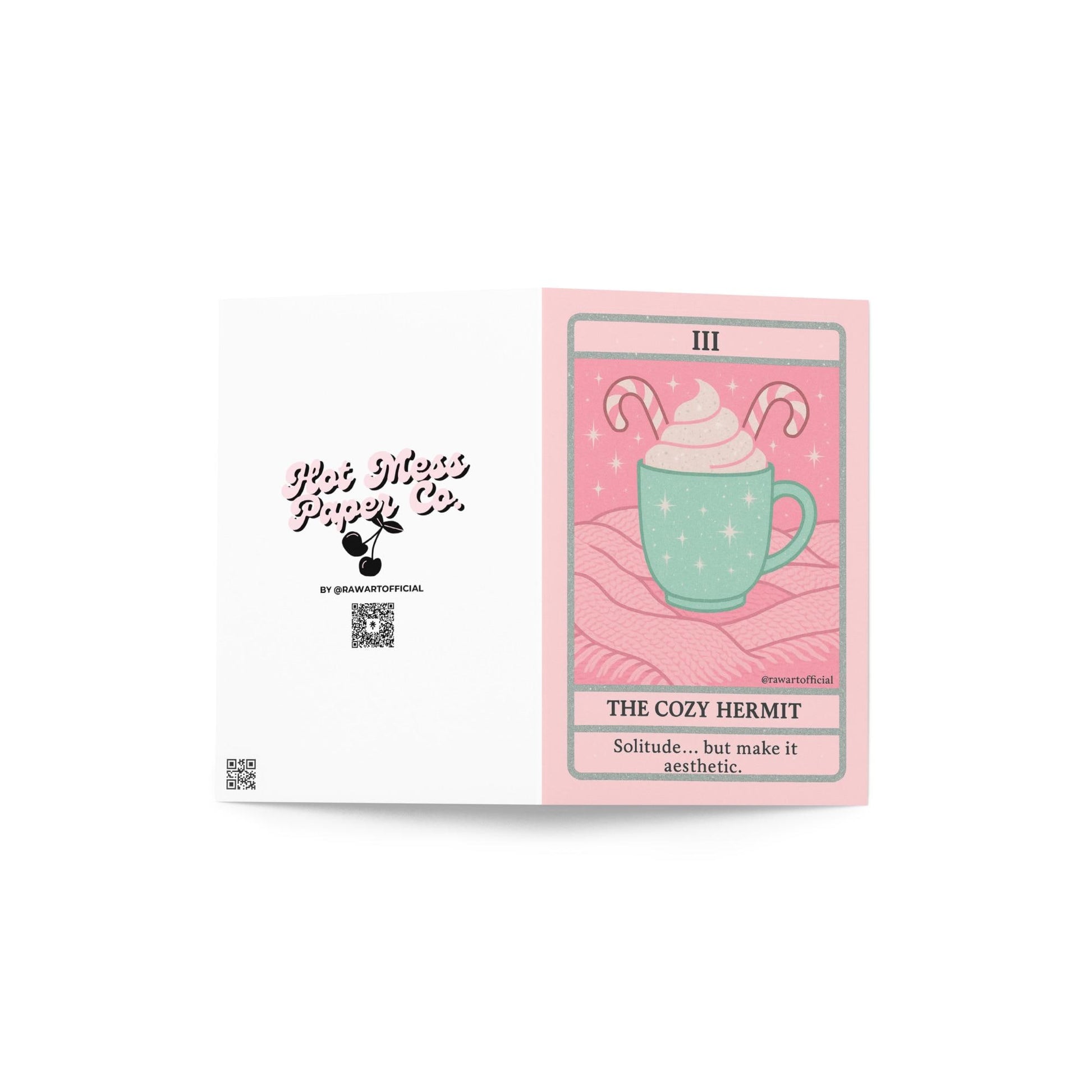 Pastel pink and mint Christmas tarot-style card featuring a mint green mug topped with whipped cream and candy canes on a pink knit blanket, titled “The Cozy Hermit” with the phrase “Solitude… but make it aesthetic.”