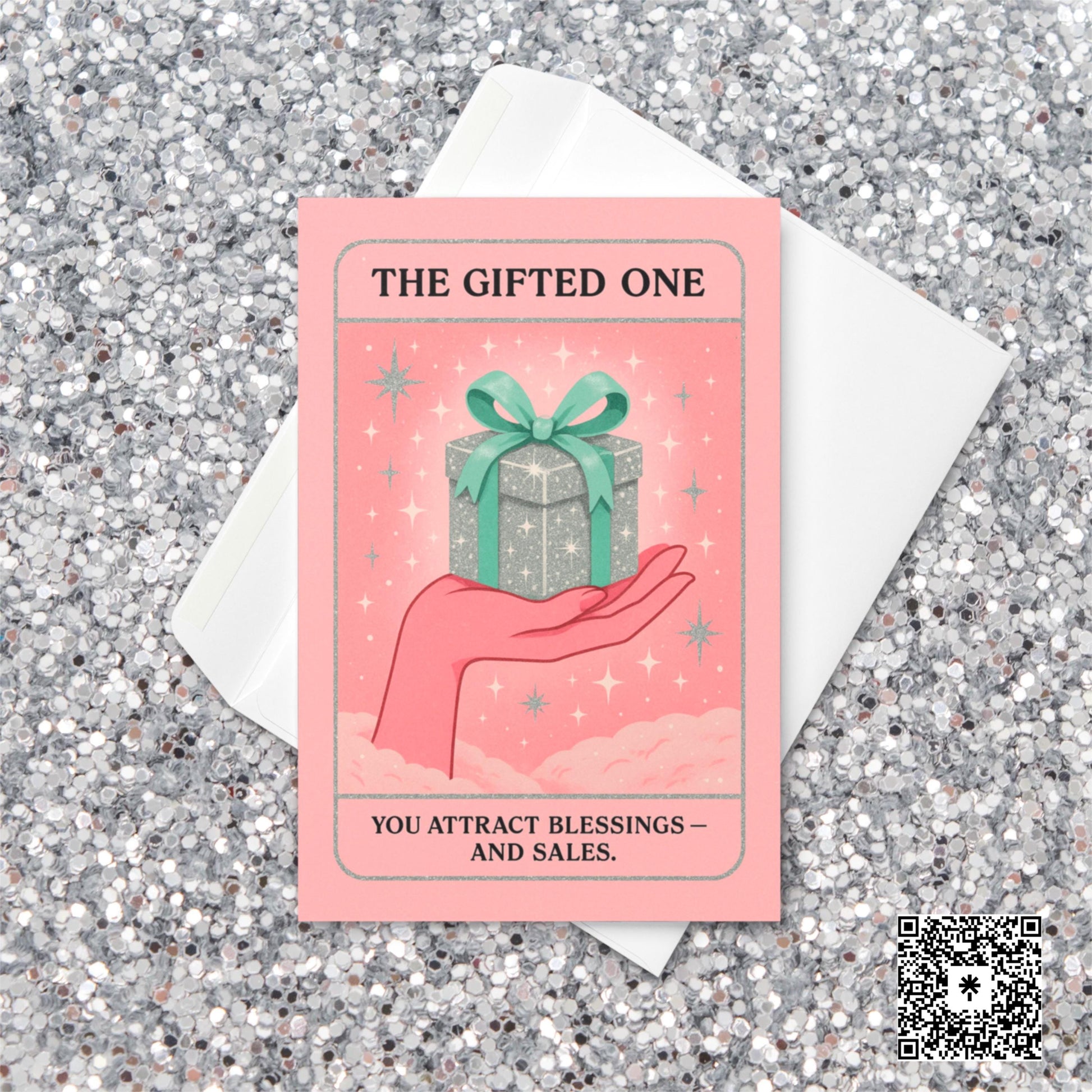 Pastel pink and mint Christmas tarot-style card featuring a sparkling silver gift box with a green bow resting on an illustrated hand, with the text “The Gifted One – You attract blessings and sales.”