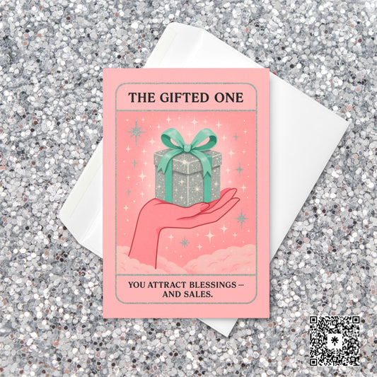 Pastel pink and mint Christmas tarot-style card featuring a sparkling silver gift box with a green bow resting on an illustrated hand, with the text “The Gifted One – You attract blessings and sales.”