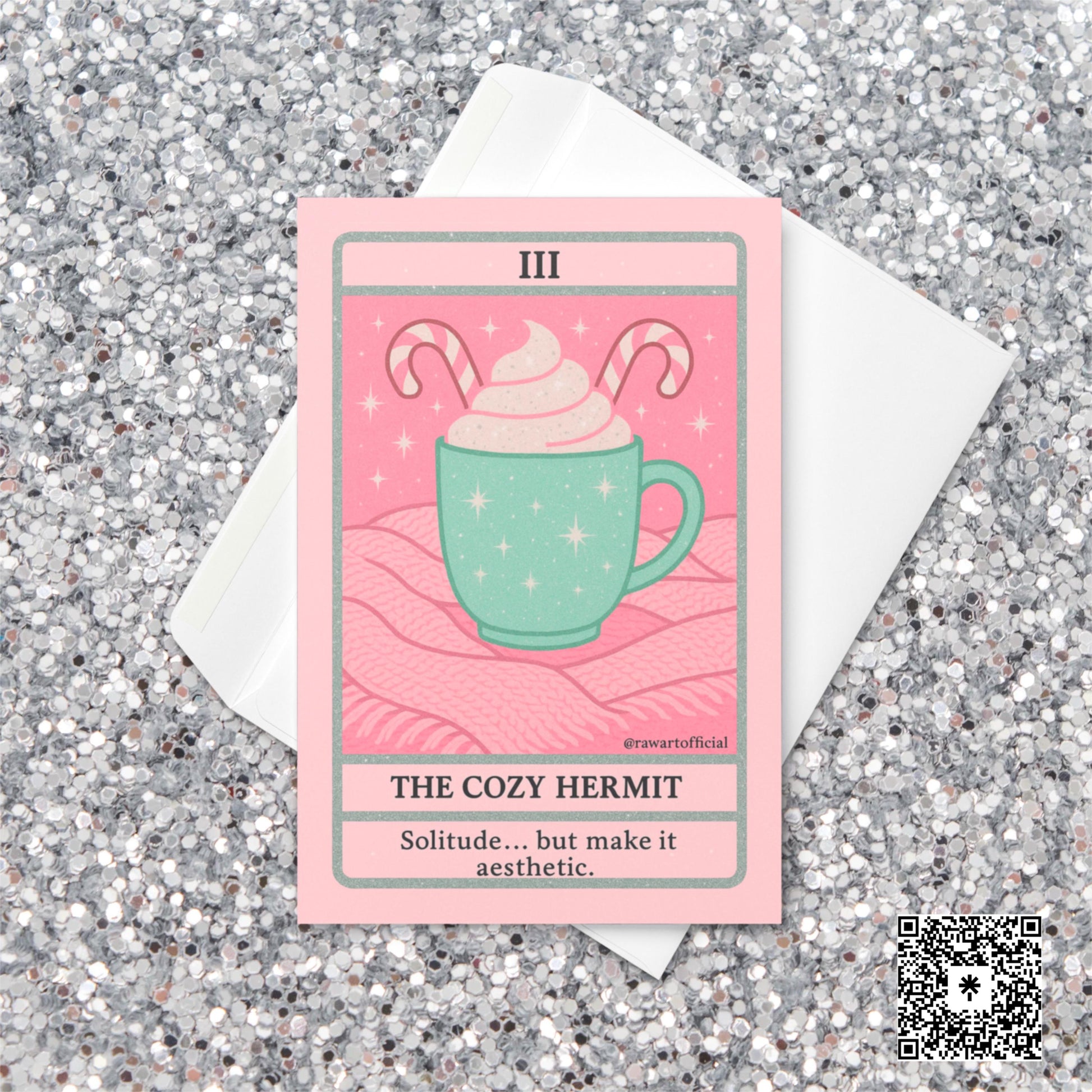 Pastel pink and mint Christmas tarot-style card featuring a mint green mug topped with whipped cream and candy canes on a pink knit blanket, titled “The Cozy Hermit” with the phrase “Solitude… but make it aesthetic.”