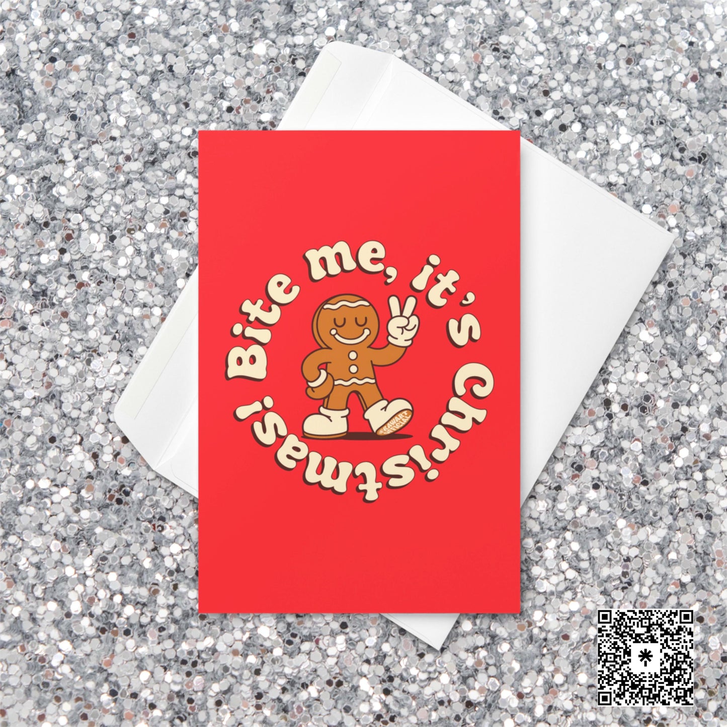 Red Christmas card featuring a smiling gingerbread man with a bite out of his leg, holding up a peace sign, surrounded by cream text reading “Bite me, it’s Christmas!”