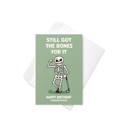 Funny golf birthday card showing a flexing cartoon skeleton holding a golf club with the words “Still Got the Bones for It” and “Happy Birthday” on a green background.