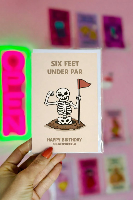 Funny golf birthday card showing a cartoon skeleton flexing inside a golf hole holding a red flag with the words “Six Feet Under Par” and “Happy Birthday” on a beige background.