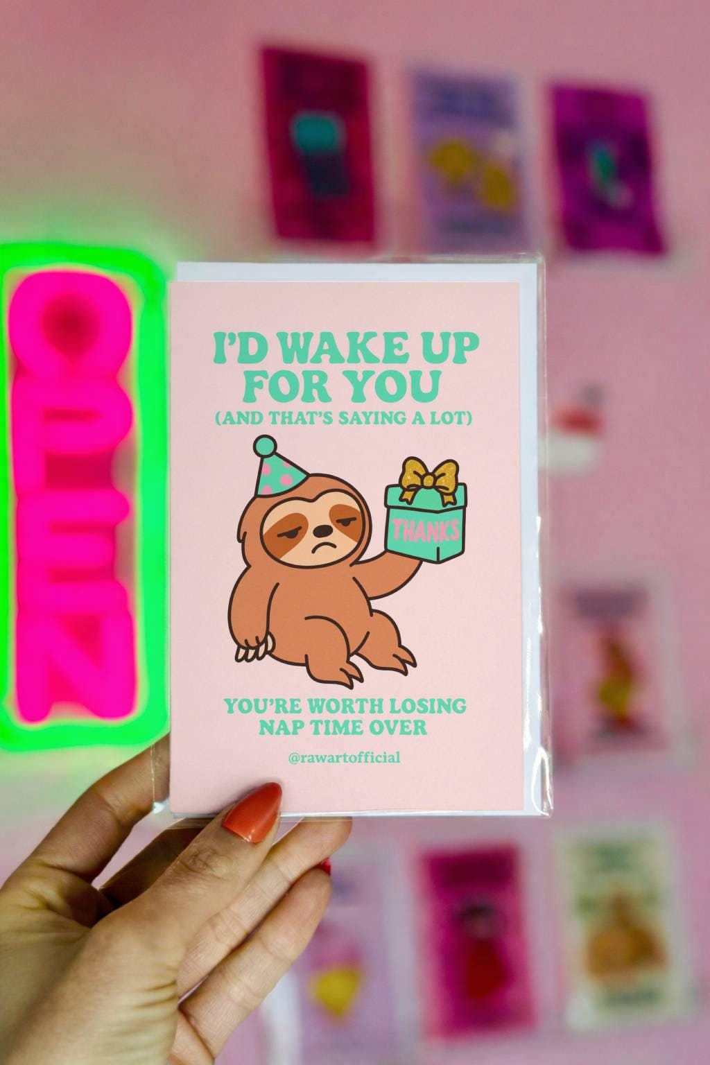 Greeting card featuring a sleepy sloth wearing a party hat holding a small gift with text about waking up and losing nap time.