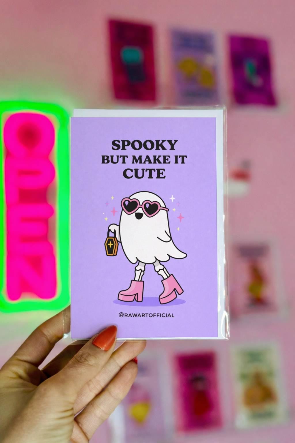 Spooky ghost greeting card with pink heart sunglasses and boots holding coffin bag on purple background with “Spooky but make it cute” text