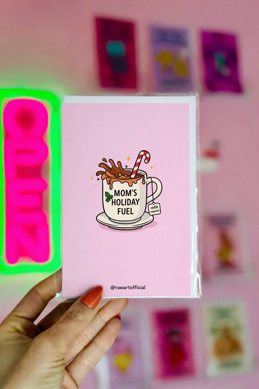 Funny Christmas card for mom with coffee mug reading “mom’s holiday fuel” and candy cane on pink background