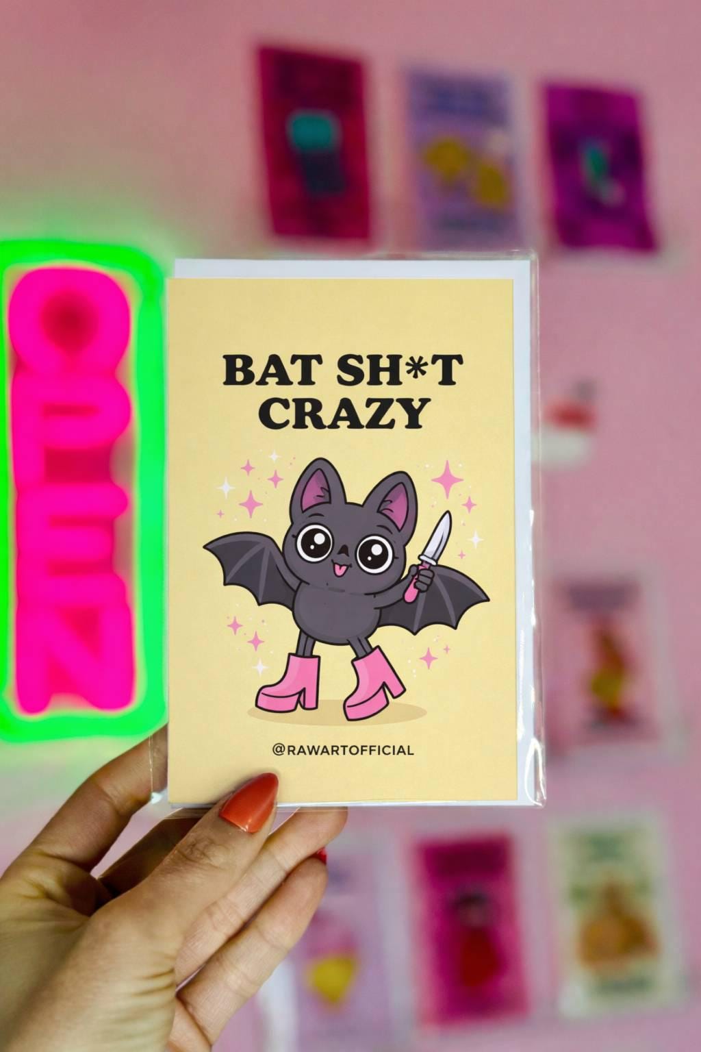 Spooky bat greeting card with cute bat holding knife and text “Batshit Crazy” on yellow background