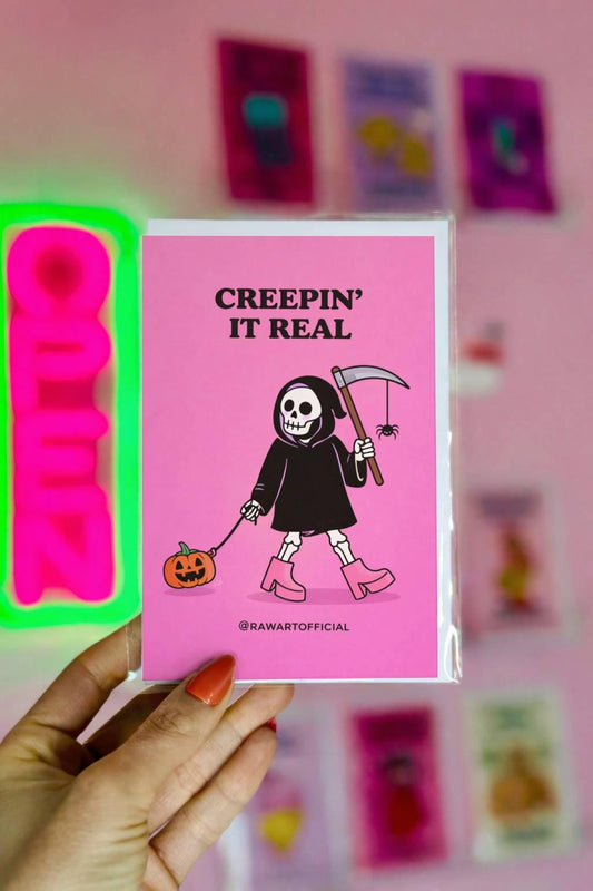 Funny spooky greeting card with skeleton holding scythe and pumpkin, text “creepin it real” on pink background