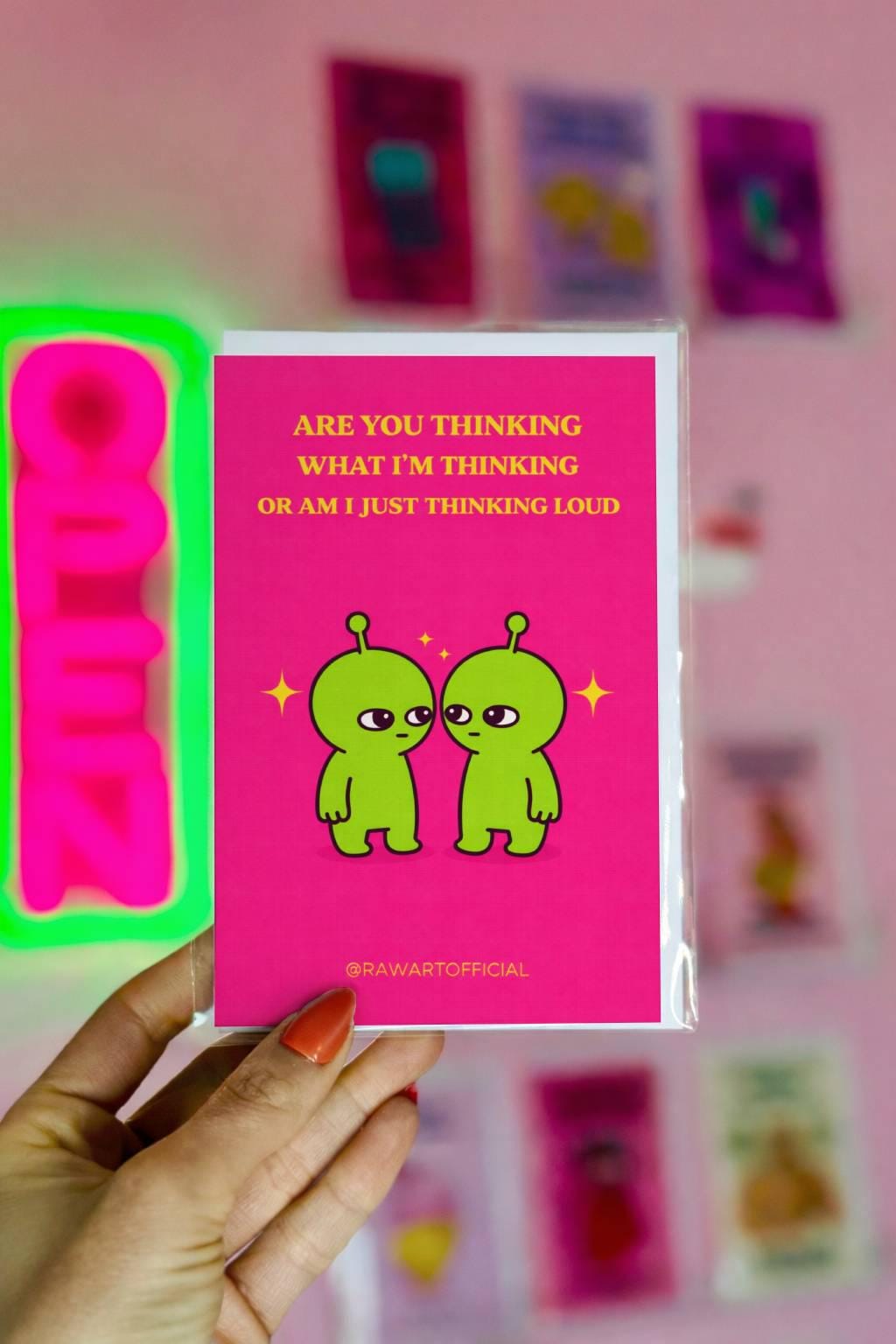 Funny greeting card with two green aliens facing each other, text reads “Are you thinking what I’m thinking or am I just thinking loud” on pink background