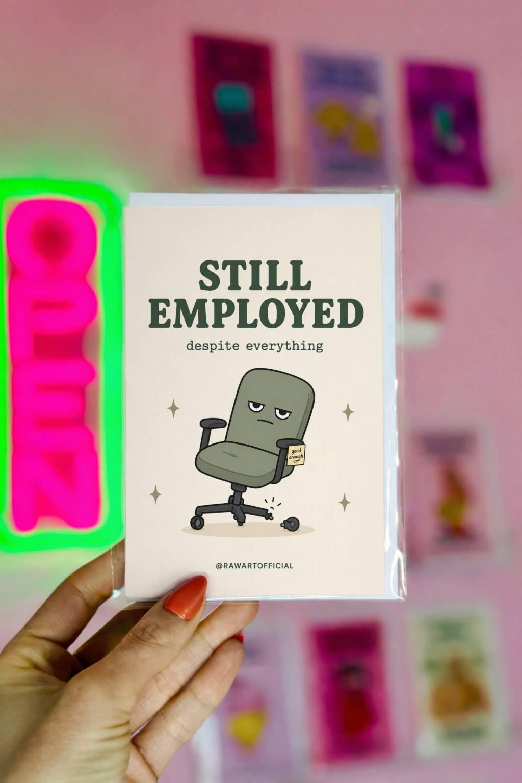 Funny coworker birthday card with broken office chair, text says “still employed despite everything”