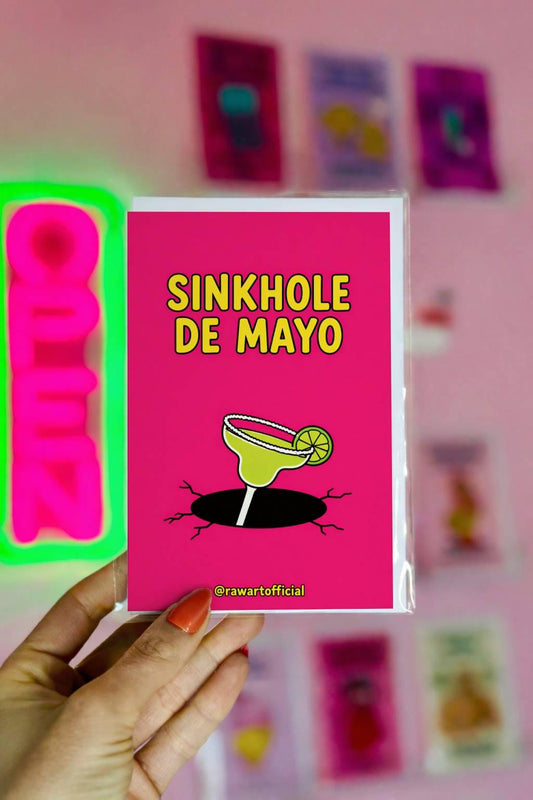 Funny Cinco de Mayo greeting card with a margarita falling into a sinkhole and text “Sinkhole De Mayo” on a pink background