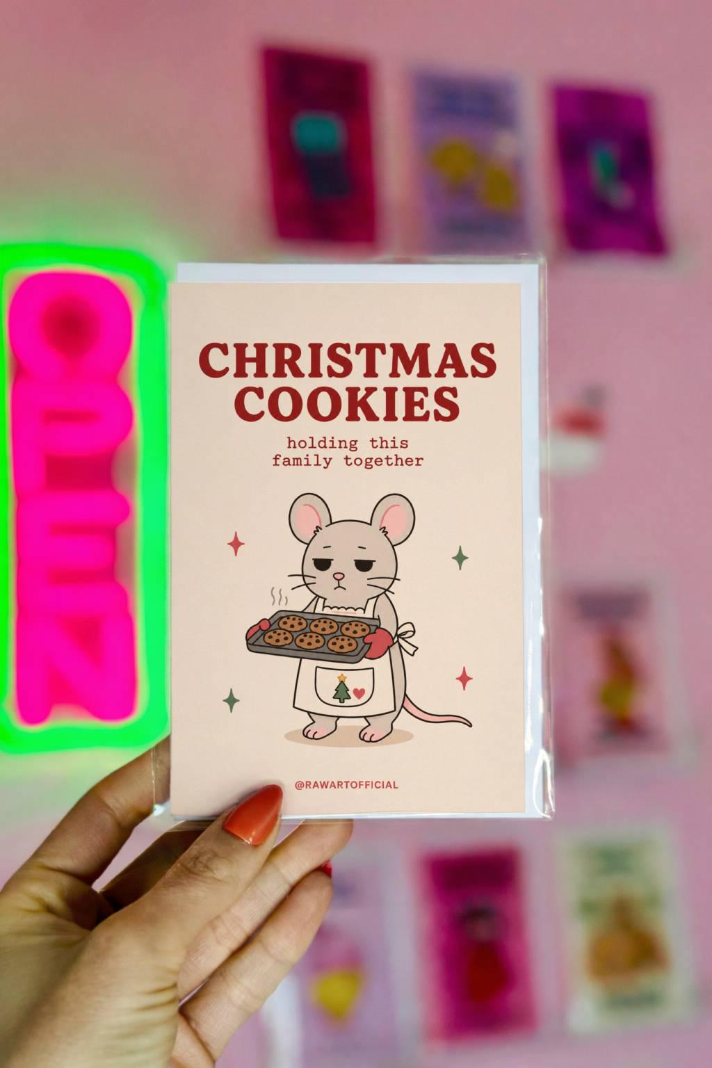Funny Christmas greeting card with tired mouse holding tray of cookies on cream background saying “Christmas Cookies Holding This Family Together”