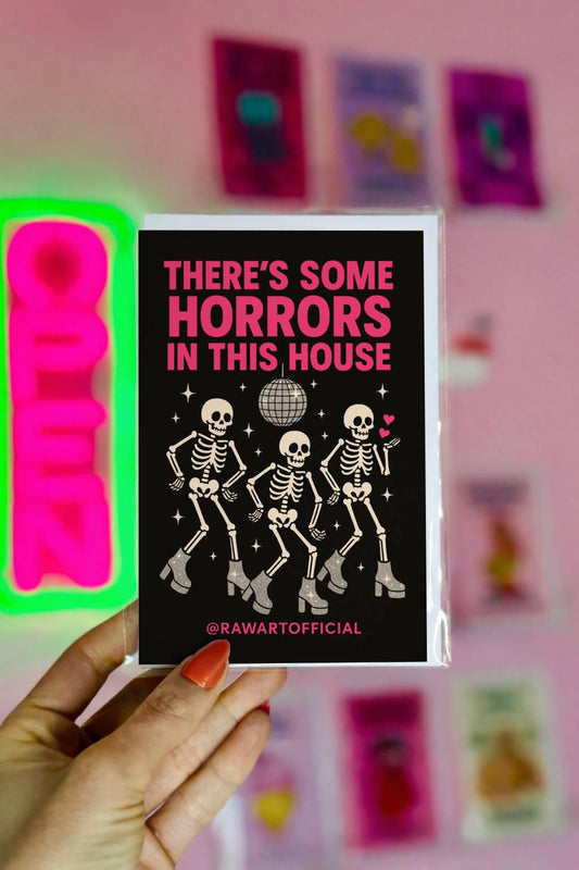 Funny Halloween greeting card with three dancing skeletons in sparkly boots and disco ball on black background saying “There’s Some Horrors in This House”
