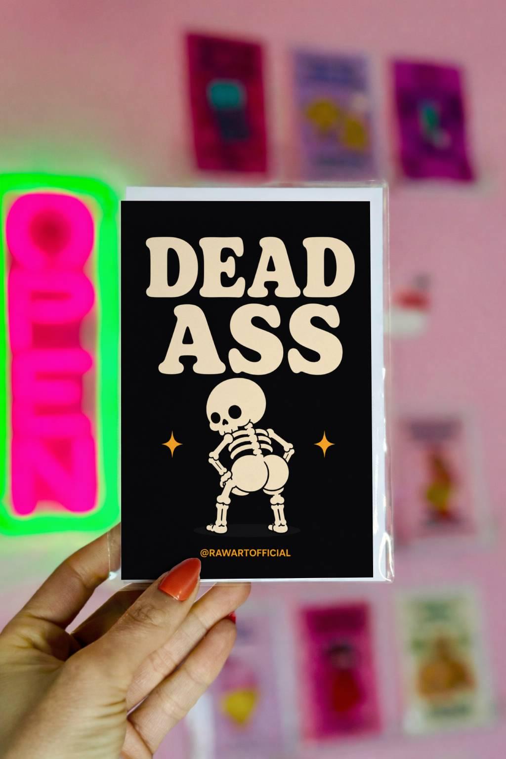 Funny Halloween greeting card with cheeky dancing skeleton booty on black background saying “Dead Ass” in bold retro lettering.