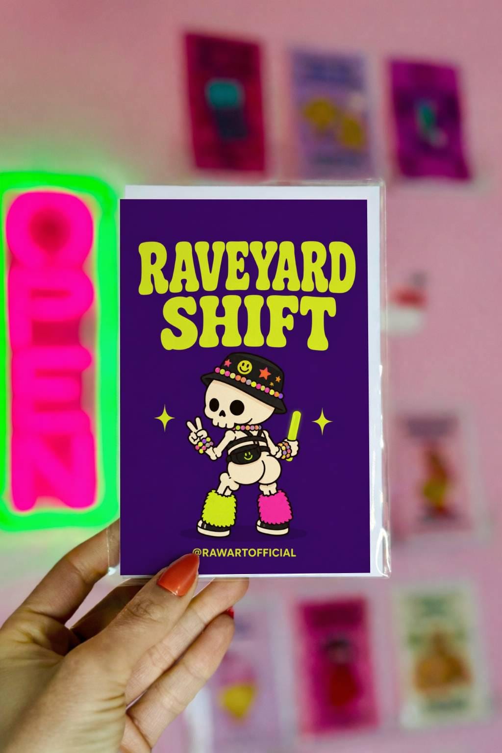 Funny Halloween greeting card with cheeky rave skeleton wearing kandi and fuzzy leg warmers saying “Raveyard Shift” on purple background.