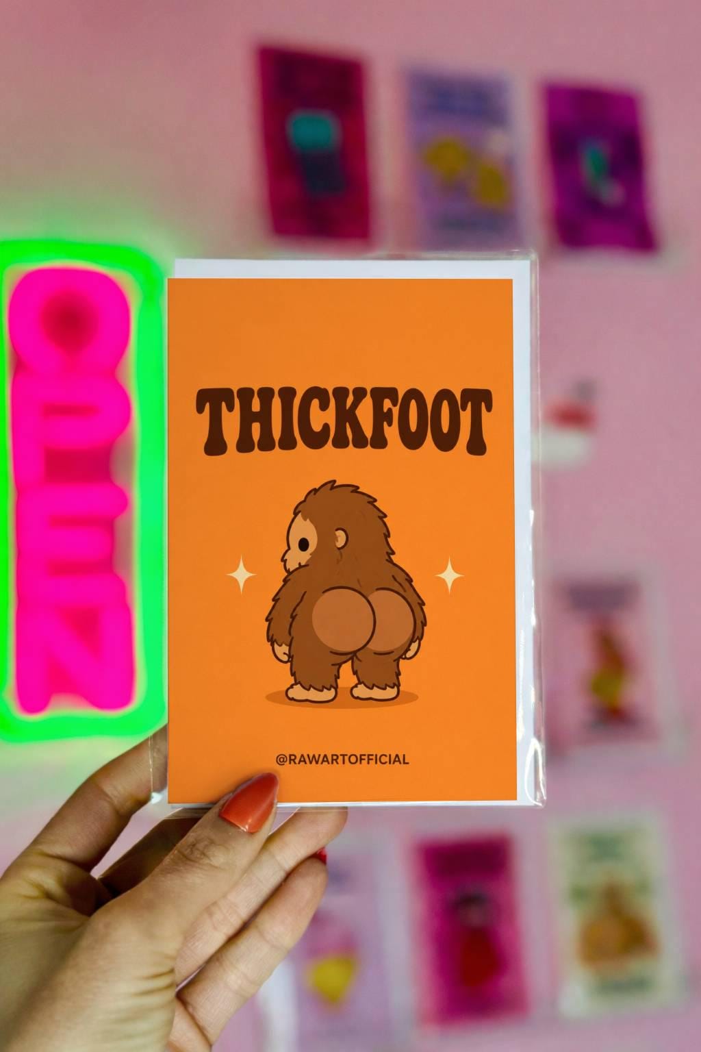 Funny Halloween greeting card with cheeky Bigfoot booty on orange background saying “Thickfoot” in retro lettering.