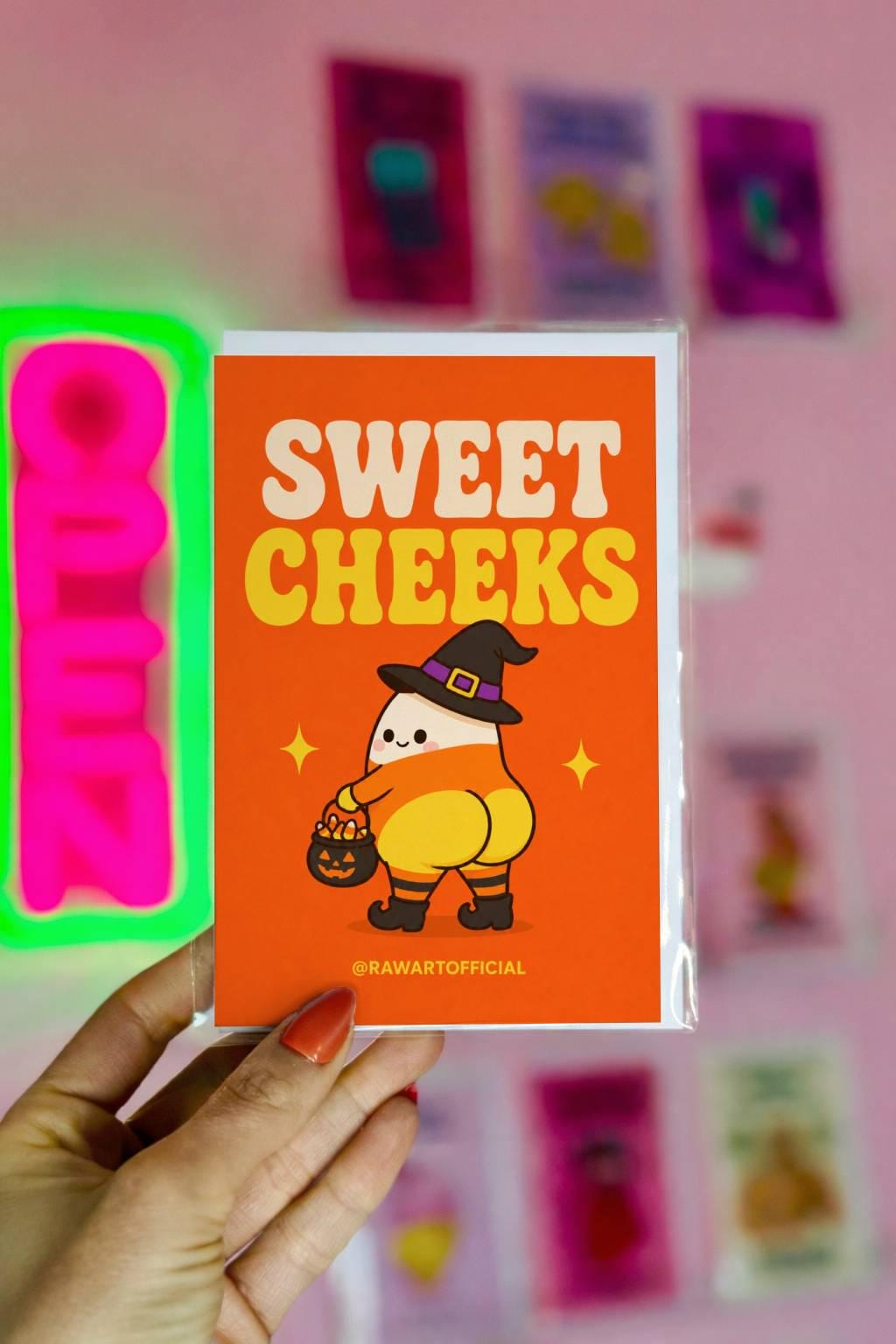 Funny Halloween greeting card with cute candy corn witch character holding candy bucket and text reading “Sweet Cheeks” on orange background.