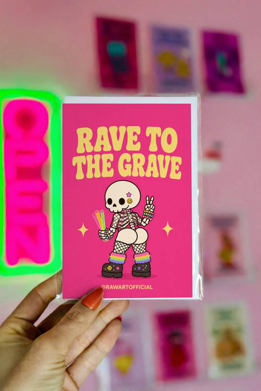Funny Halloween greeting card with cheeked-up rave skeleton holding glow sticks and text reading “Rave to the Grave” on hot pink background.